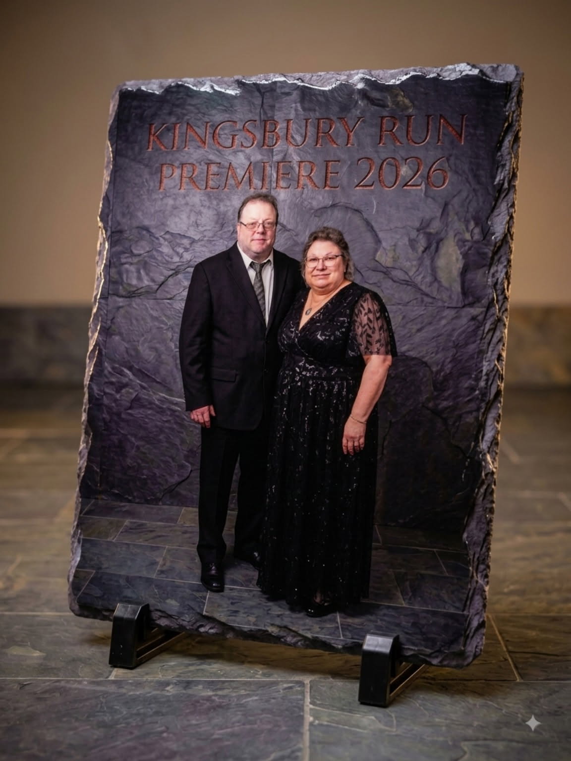 A couple standing with a large stone-textured display of their finished piece at an event
