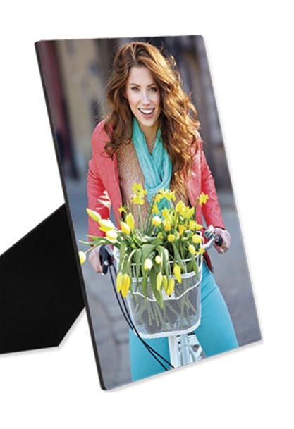 A printed photo panel on a small black easel stand — a smiling woman riding a bicycle with a basket of yellow tulips — one of the wood photo panels Albritton's Art™ is preparing to offer